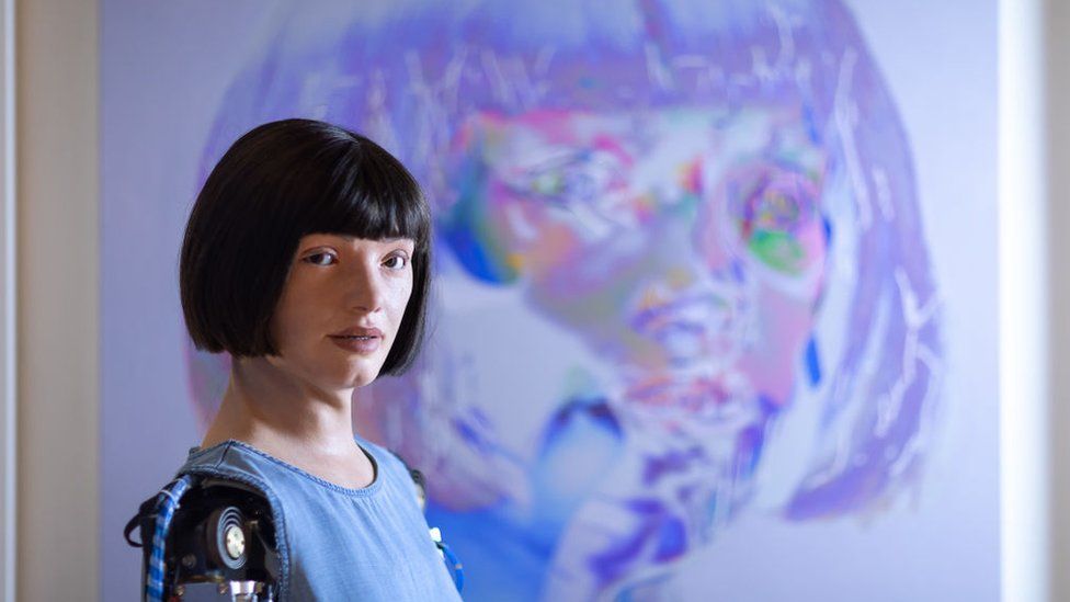 Image caption, Ai-Da stands in front of one of 'her' artworks.