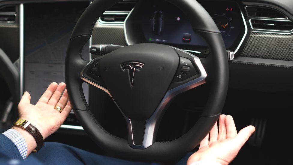 Водитель снимает руки с руля автомобиля марки Tesla