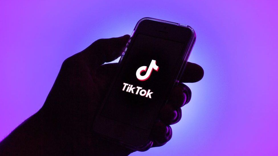 Холокост. An illustration of a hand holding a phone showing the TikTok logo