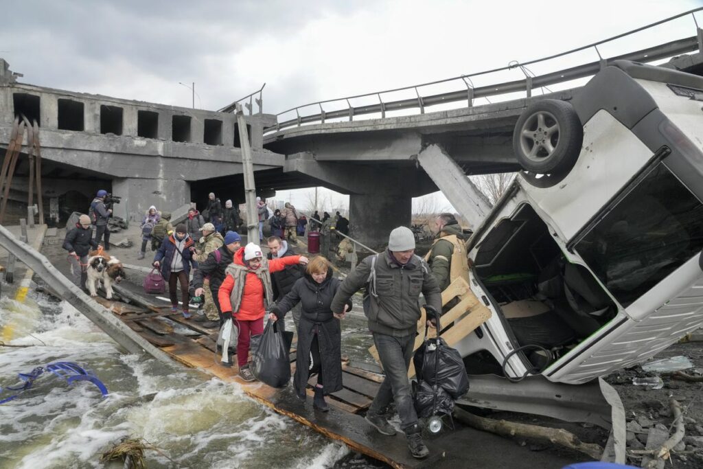 Люди переходят по импровизированному пути под разрушенным мостом, покидая город Ирпень в марте.
