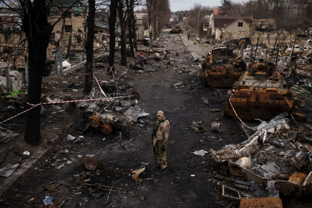 Украинский военнослужащий стоит на фоне уничтоженных российских танков в Буче, на окраине Киева, Украина, среда, 6 апреля 2022 года.
