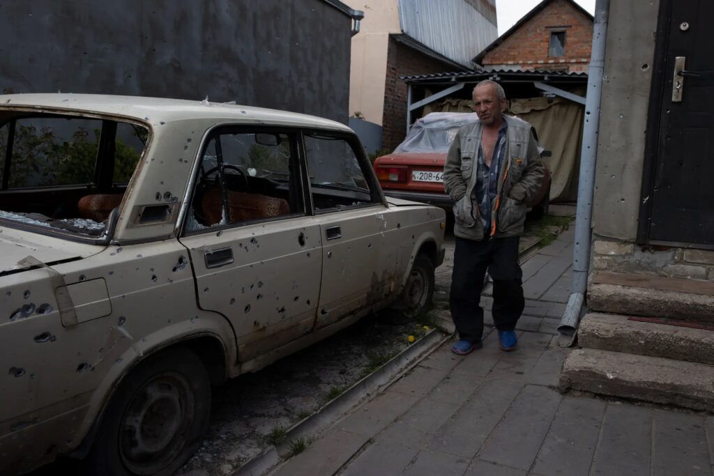 Одна деревня зараз: артиллерийская война в Украине 3 Житель Руска Лозова рядом с автомобилем, разбитым во время перестрелки.