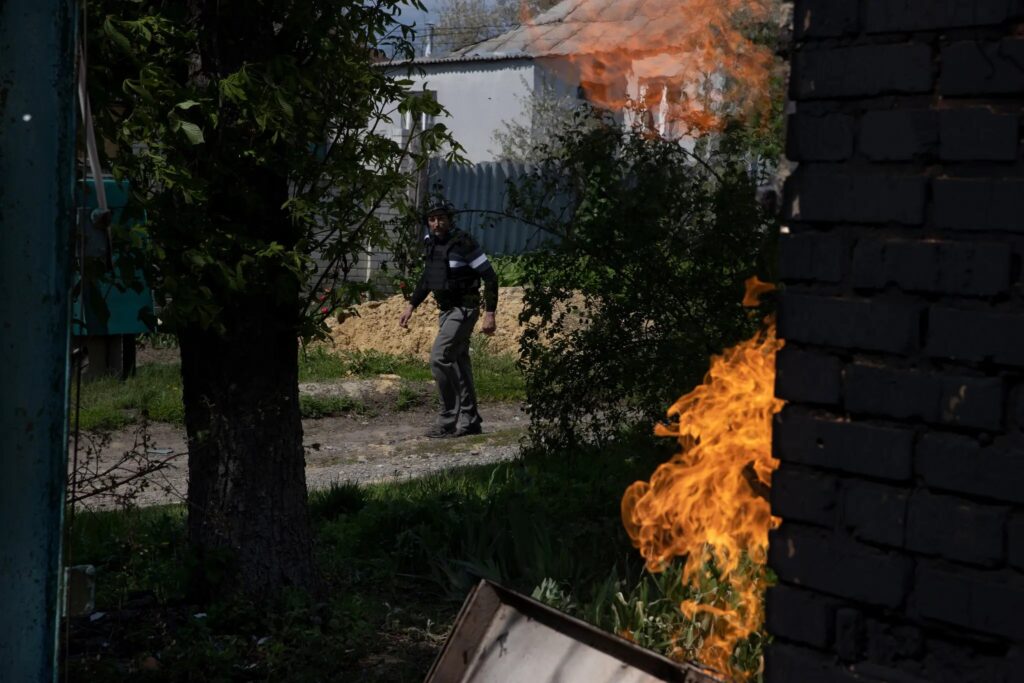 Артиллерийская война в Украине. Олег, строитель, ставший добровольцем, проходит мимо горящего дома в поисках эвакуированных жителей в Руской Лозовой, Украина.