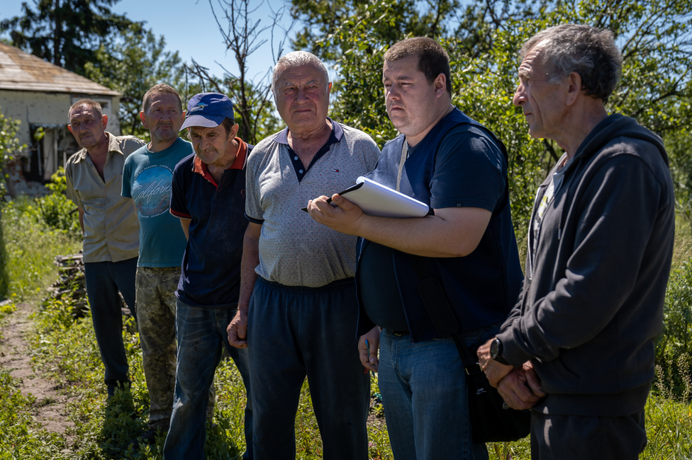, Vadym Bobaryntsev, right, watches with other villagers as a police officer takes notes.