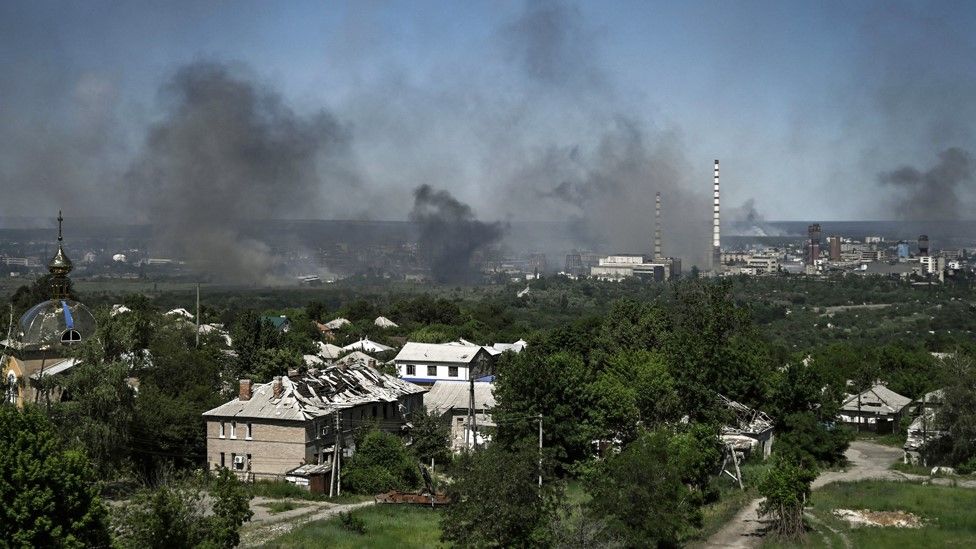 , A damaged building can be seen in Lysychansk as black smoke rises from the nearby city of Severodonetsk