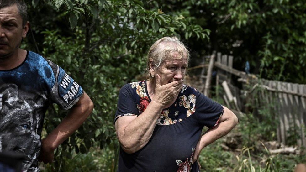 , A woman stands near a destroyed house in Luhansk, where Russia is intensifying its attacks
