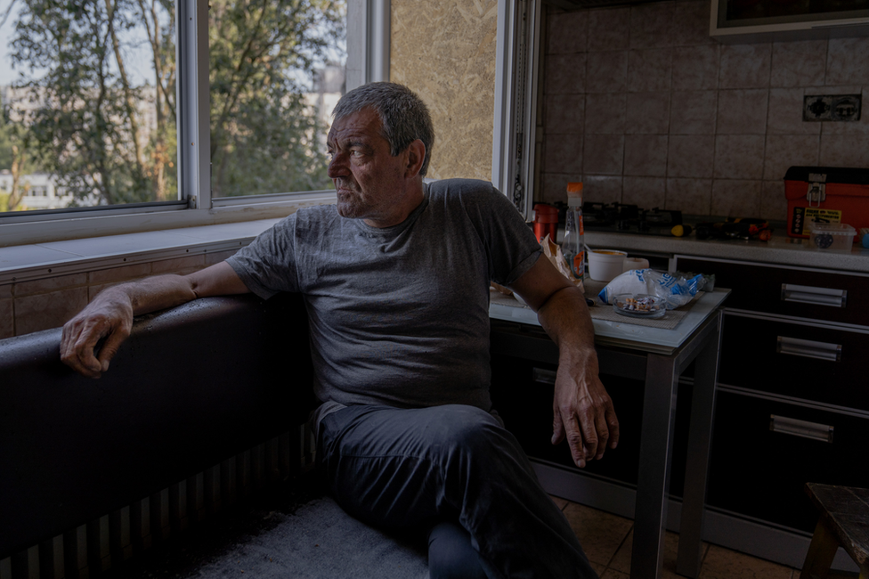 , Valeriy Ivanovych looks out from his apartment window. Only two people are left among the 18 apartments in this side of the building