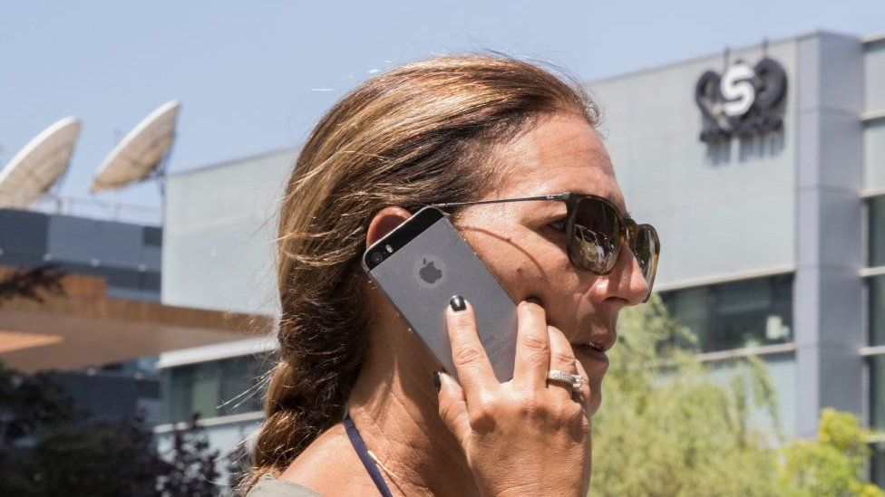 , A woman uses her phone outside the offices of NSO