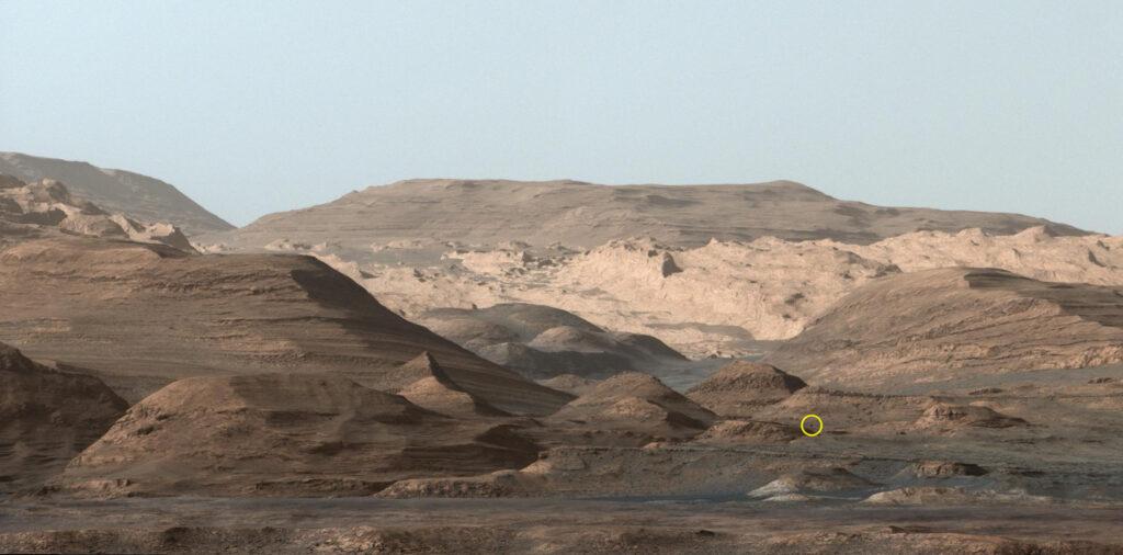 Перевал Парайтепуй с расстояния: Эта сцена была запечатлена Curiosity 9 сентября 2015 года, когда марсоход НАСА находился за много миль от своего нынешнего местоположения. Круг указывает на местоположение валуна размером с Кьюриосити, мимо которого недавно проехал марсоход. Слева от него находится "Перевал Парайтепуй", через который Curiosity сейчас проезжает. 