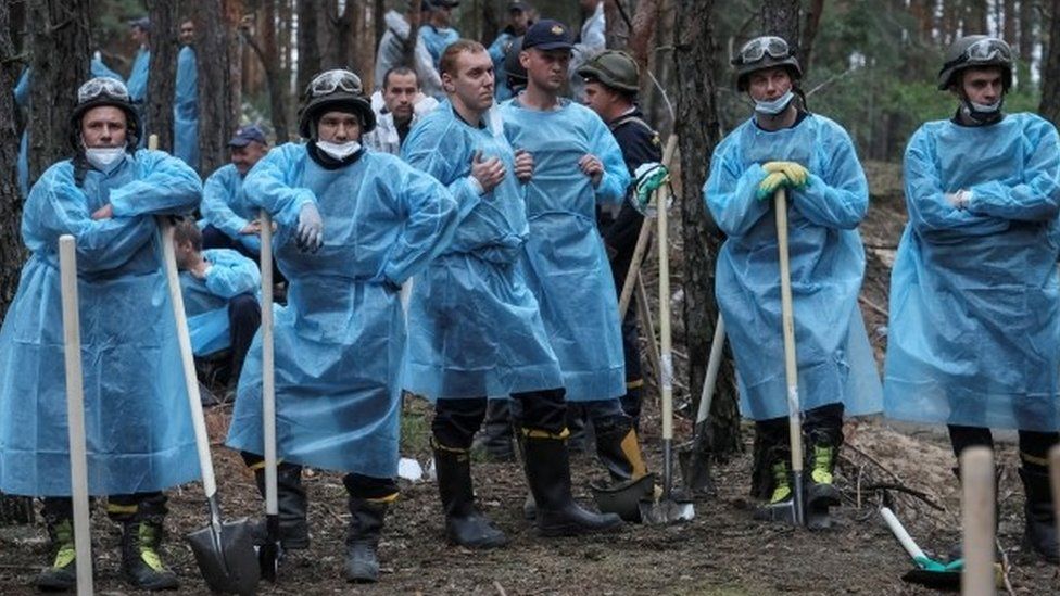 Изюм. Работники экстренных служб были одеты в синие пластиковые накидки, когда копали землю