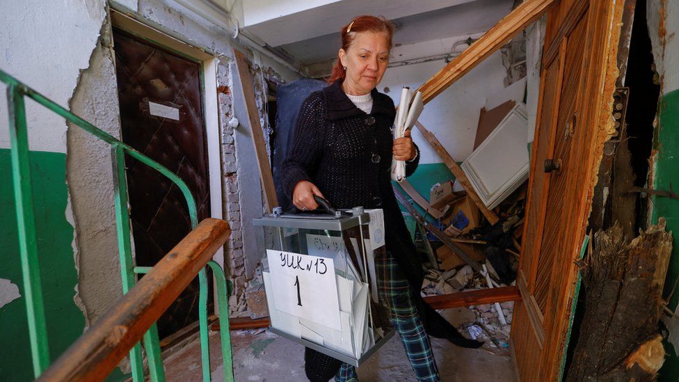 An electoral worker carries a ballot box through a war-damaged block of flats in Mariupol, Donetsk region