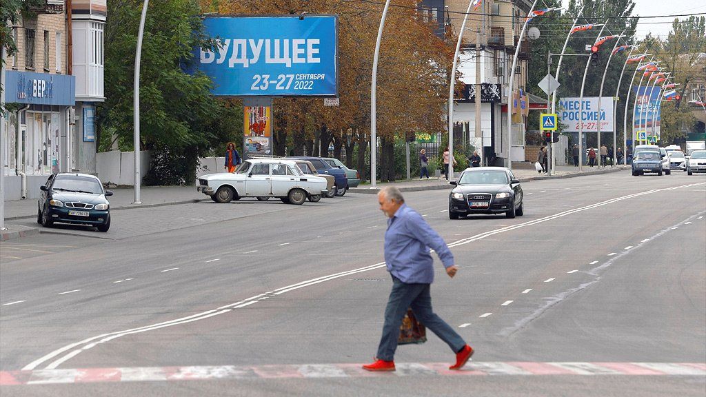 A man crosses a Melitopol street on 26 September 2022. A banner in the background promotes the Moscow-backed referendum - it reads: "Future - 23-27 September 2022"