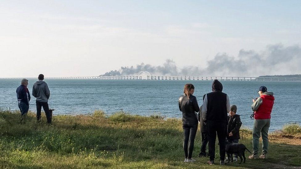 People watch fuel tanks ablaze and damaged sections of the bridge in the Kerch Strait, Crimea, on 8 October 2022