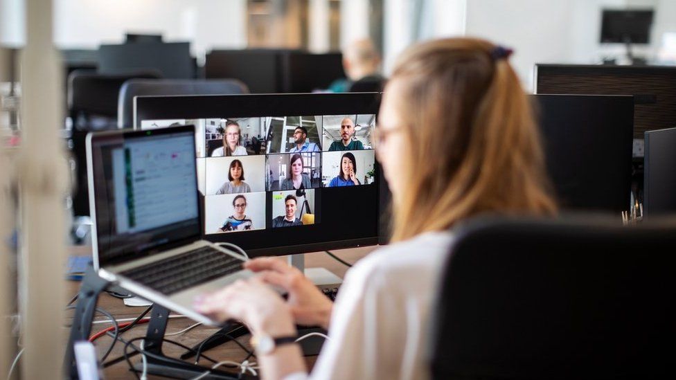 Rear view of a woman sitting in an office on a video call with team members