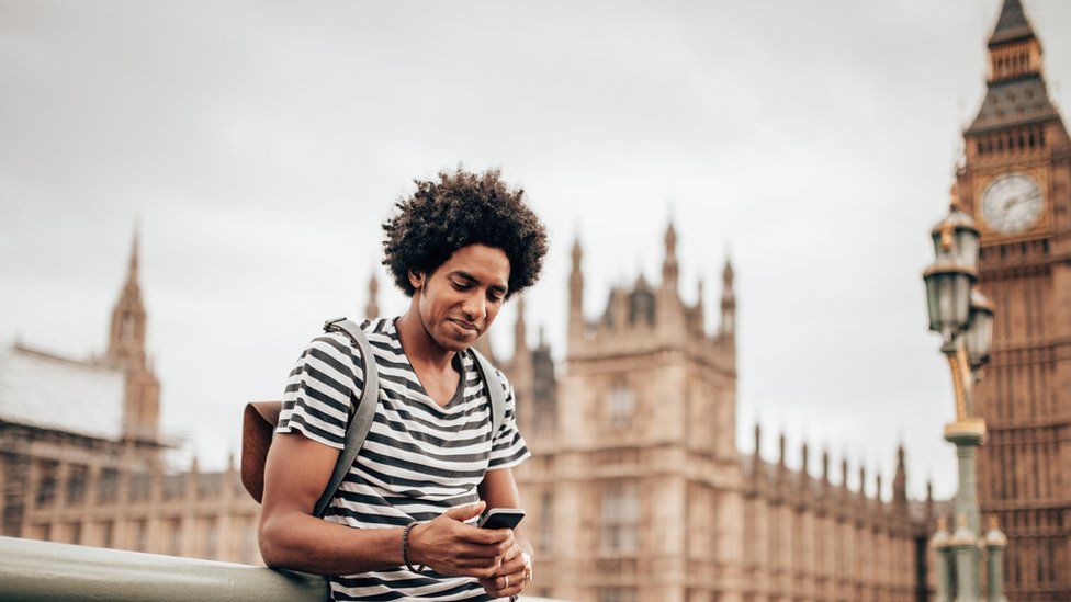A man using a smart-phone outside the houses of parliament.