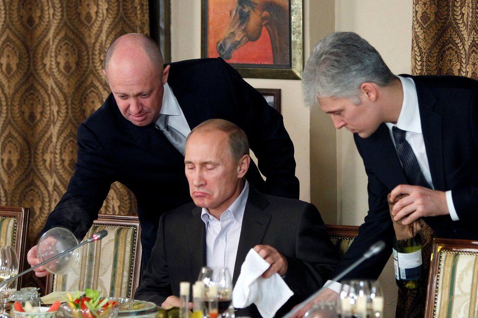 A November 2011 photo shows Yevgeny Prigozhin (L) assisting Vladimir Putin at a banquet near Moscow