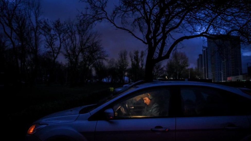 A Ukrainian woman sits in a car after the lights are turned off in Kyiv as part of scheduled power cuts