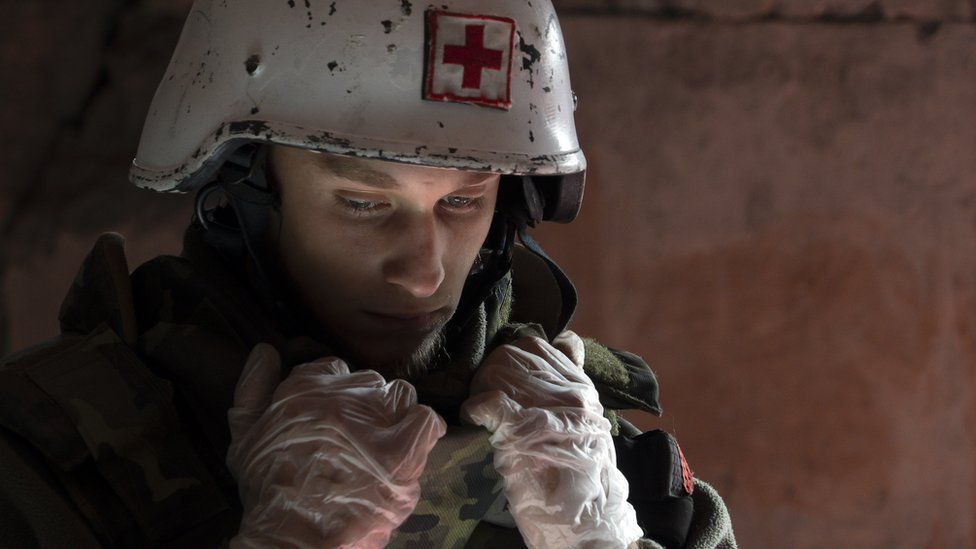 Denys wearing a white helmet with a red cross on it. The atmosphere is sombre and he's looking pensive.