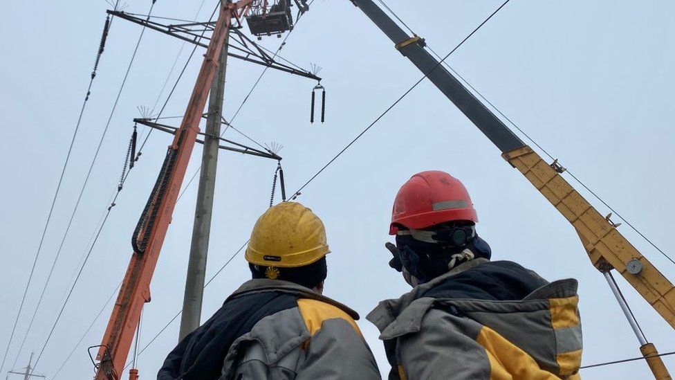 Two men in hard hats looking at a pylon