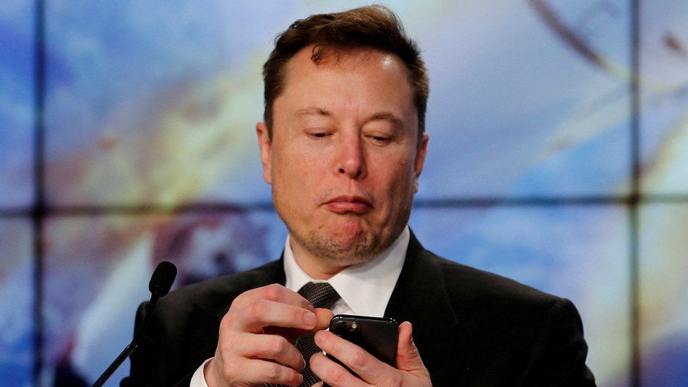 Elon Musk looks at a phone