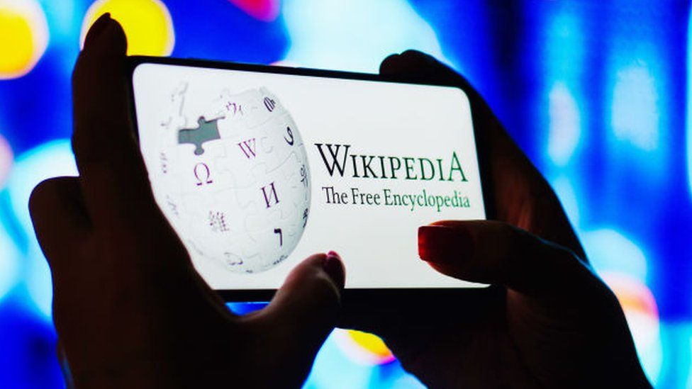 A woman holding a smartphone with Wikipedia on the screen