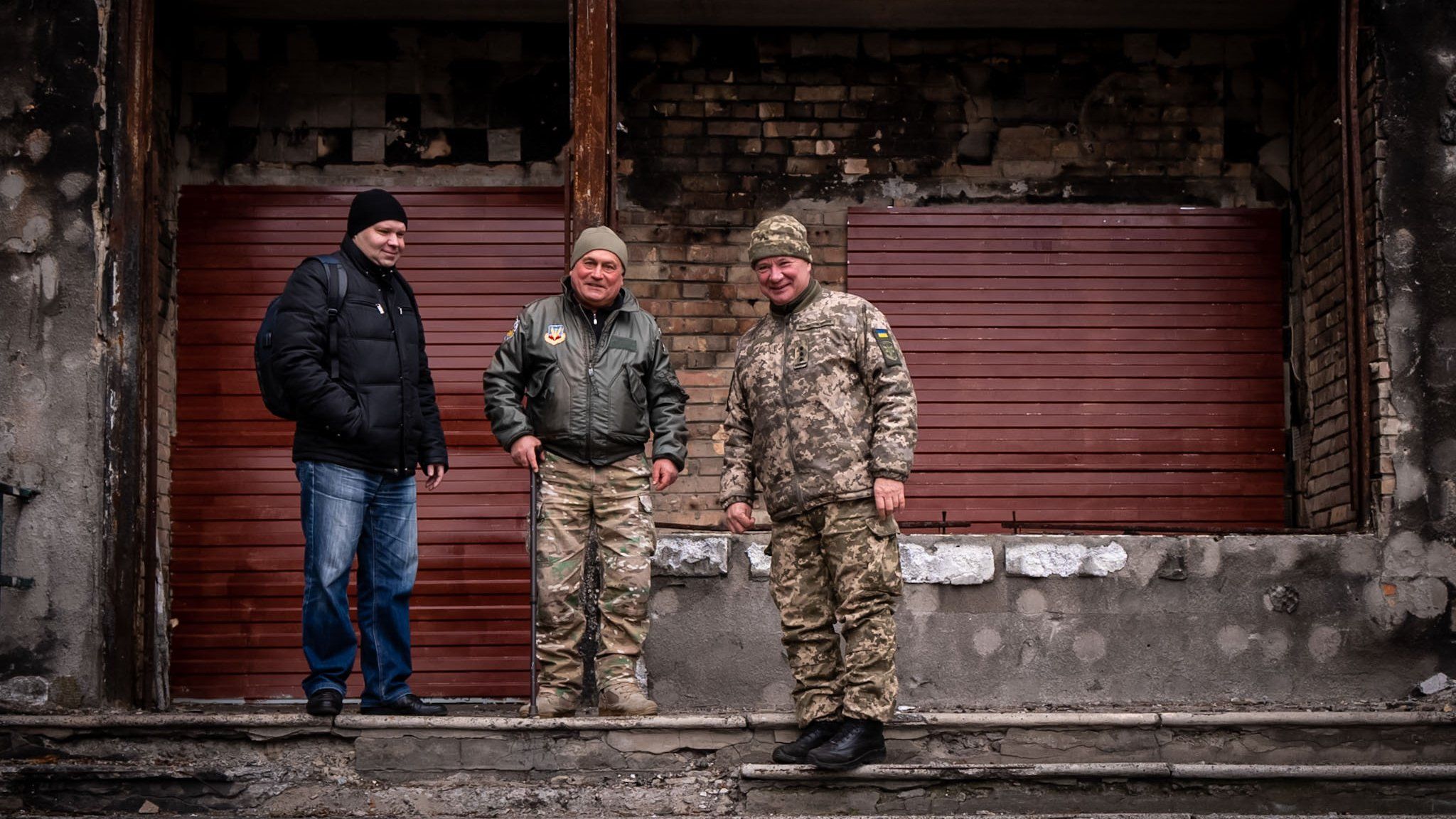 Maksym (L) Volodymyr (C) and '"the colonel" (R) stand in front of their bombed out office for local volunteers