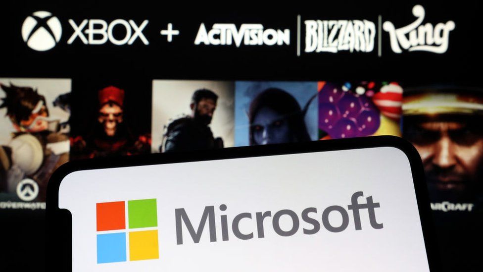 Microsoft logo displayed on a smartphone against a background showing Activision Blizzard and King titles
