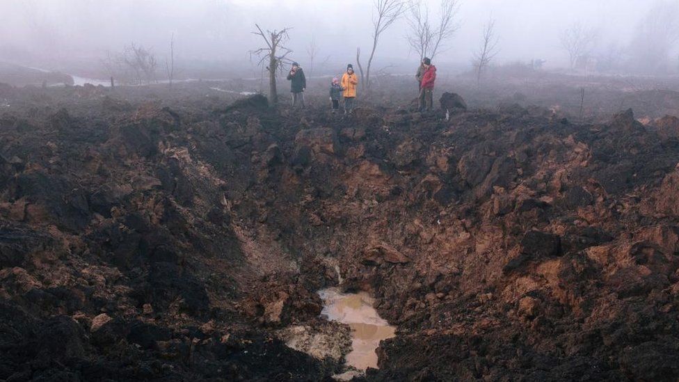 Locals gather around a shelling crater after a rocket hit the Pisochyn neighbourhood outside Kharkiv