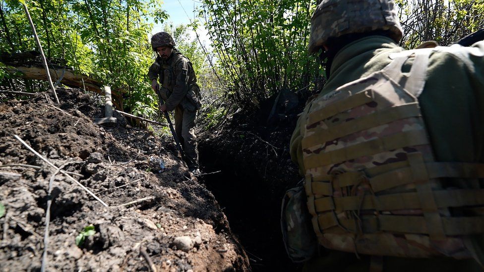 Ukrainian troops seek cover behind bushes on the outskirts of the city of Bakhmut