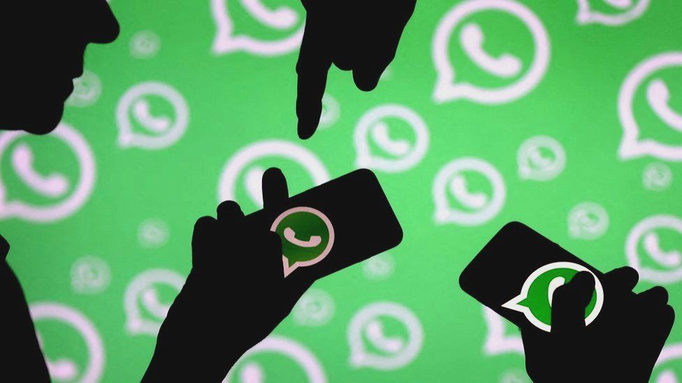Men pose with smartphones in front of displayed Whatsapp logo.