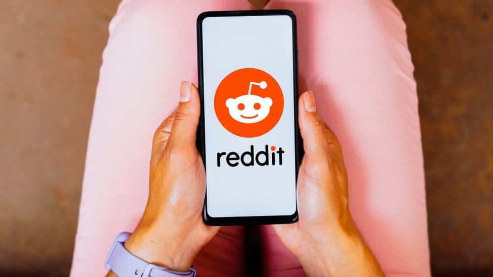 Person holding a smartphone displaying the Reddit logo