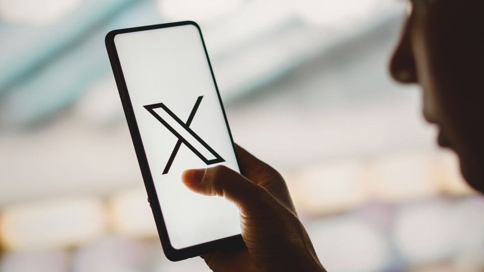 A photo illustration of someone looking at the X app on a phone