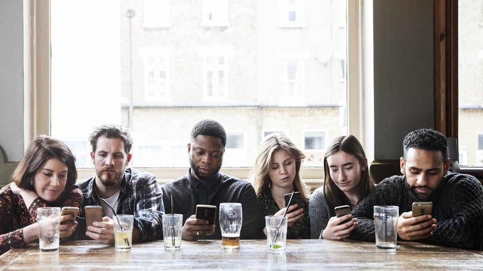 A group of people in a pub all looking at their phones (stock photograph)