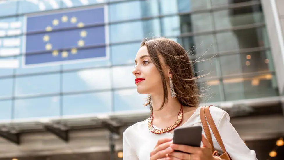 Молодая женщина с телефоном стоит возле флага ЕС