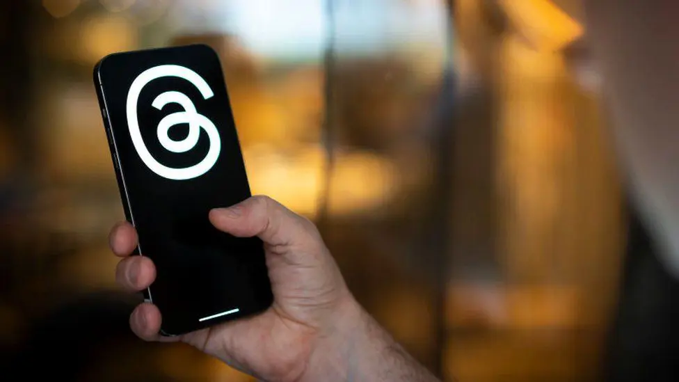Стандартная фотография человека, держащего телефон с логотипом Threads на экране