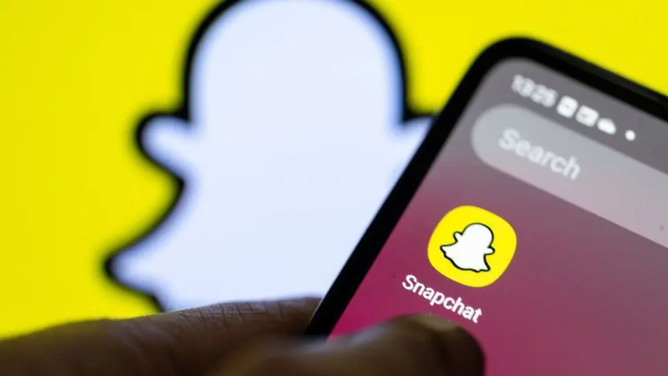 Стандартное изображение показывает приложение Snapchat на смартфоне на фоне логотипа платформы