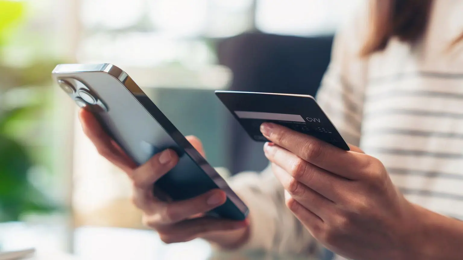 Как будет работать проверка возраста для просмотра порнографии и что будет с конфиденциальностью? 2 Женщина держит кредитную карту и мобильный телефон.