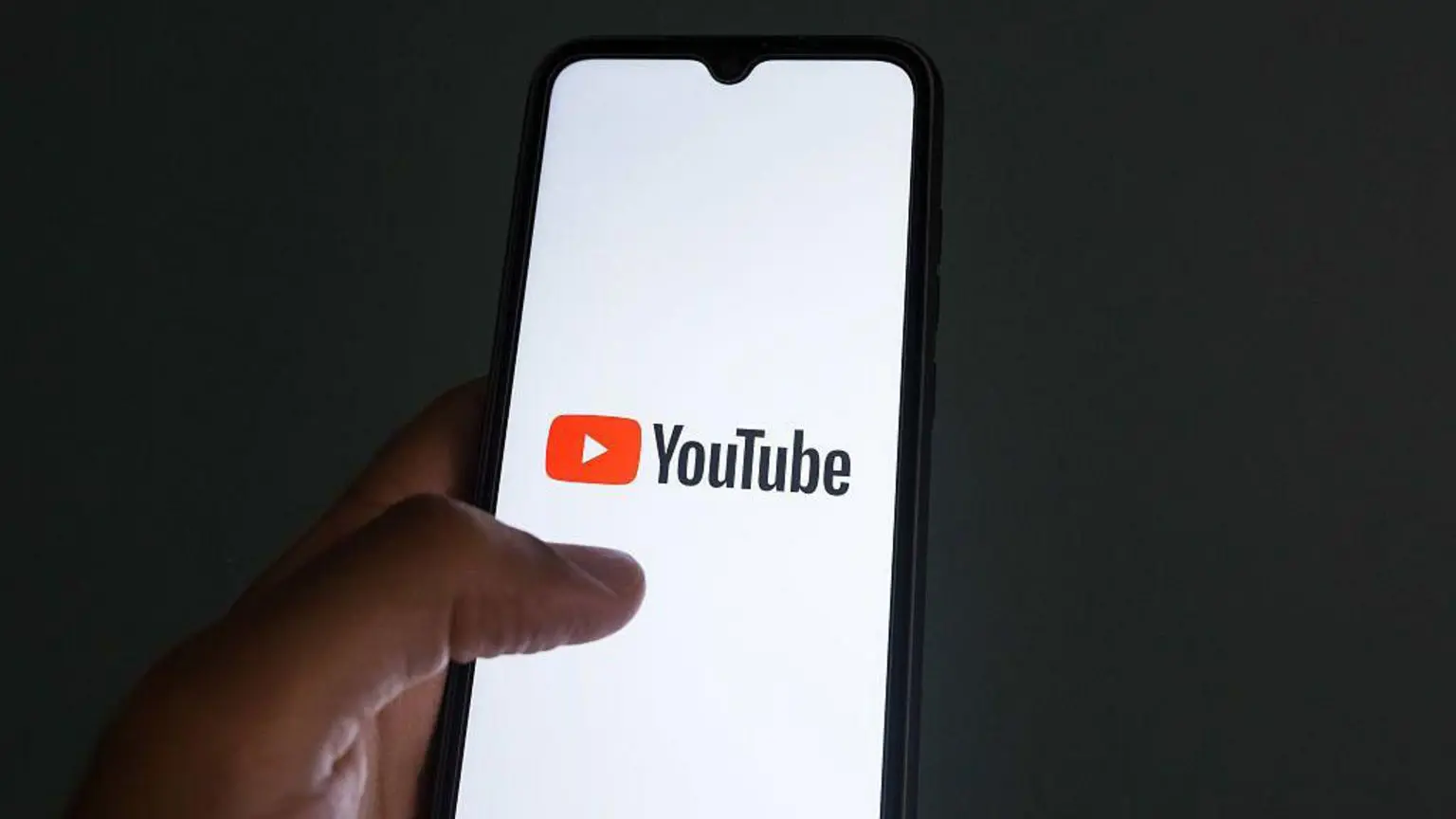 Призыв проверять рекламу на YouTube так же, как на обычном телевидении, чтобы остановить мошенничество 1 Изображение руки, держащей мобильный телефон, с логотипом YouTube.