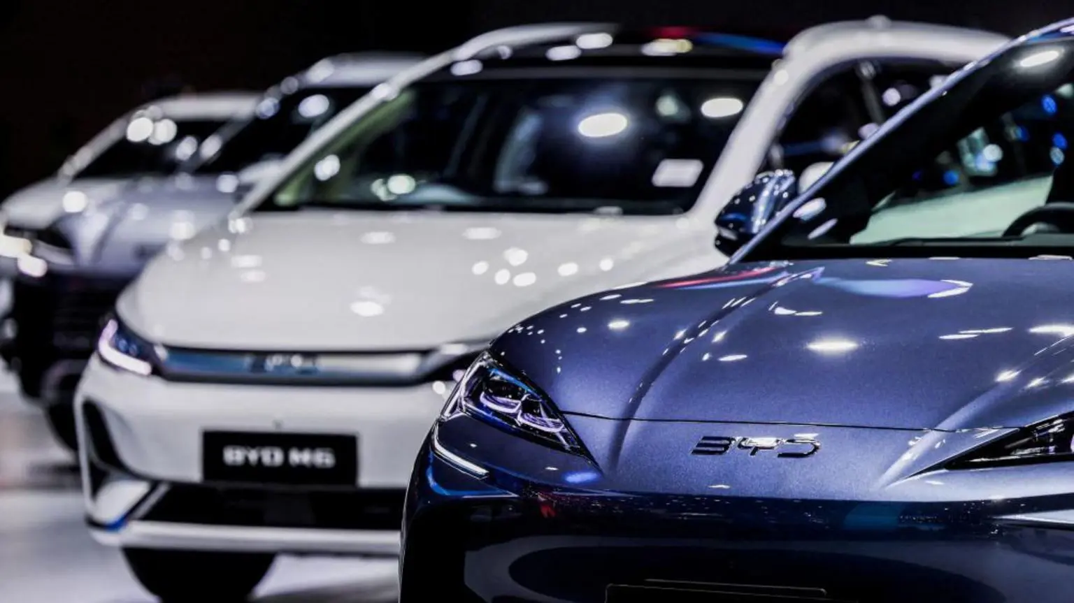 Акции BYD падают на фоне снижения прибыли из-за ценовой войны в китайском автомобильном секторе 1 На 46-м Международном автосалоне в Бангкоке, Таиланд, выставлены четыре автомобиля BYD. На переднем плане — синий седан с острыми, агрессивными фарами. За ним следует более крупный автомобиль BYD M6.