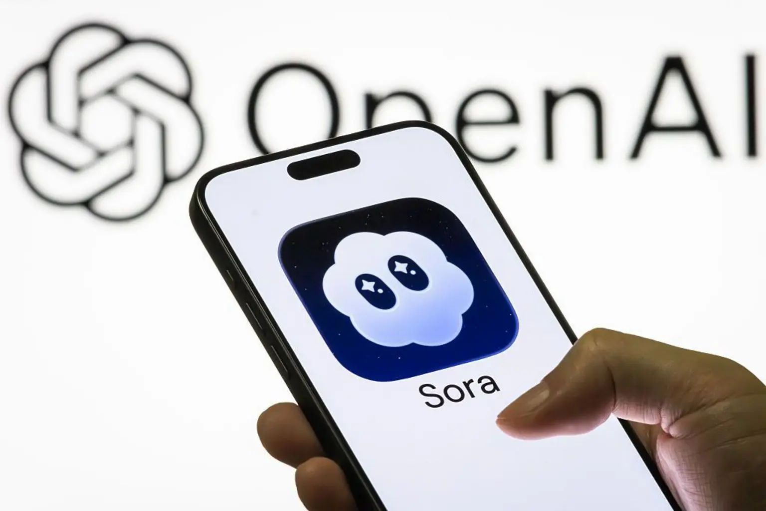 Видеоприложение OpenAI Sora достигло 1 миллиона загрузок быстрее, чем ChatGPT 1 Человек держит телефон с логотипом Sora. На экране изображено облако с глазами на белом фоне с логотипом OpenAI.