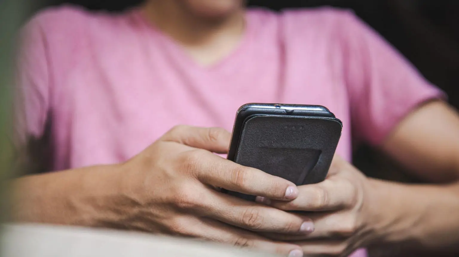 Сайт с дипфейками, демонстрирующий «обнажёнку», оштрафован на 55 000 фунтов стерлингов за отсутствие проверки возраста 1 Неопознанный человек в розовой футболке держит в руках смартфон и печатает на нём.