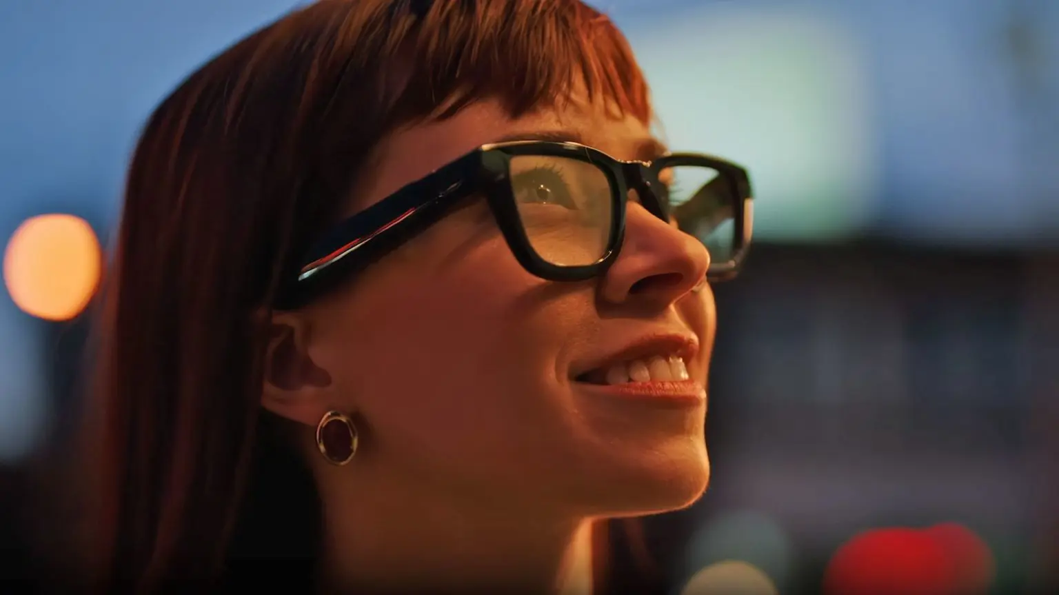 Google представила планы по возобновлению выпуска умных очков в 2026 году 1 Крупный план женщины в очках. Она улыбается, у нее длинные рыжие волосы. Очки черные, с толстой оправой, а линзы кажутся слегка прозрачными.