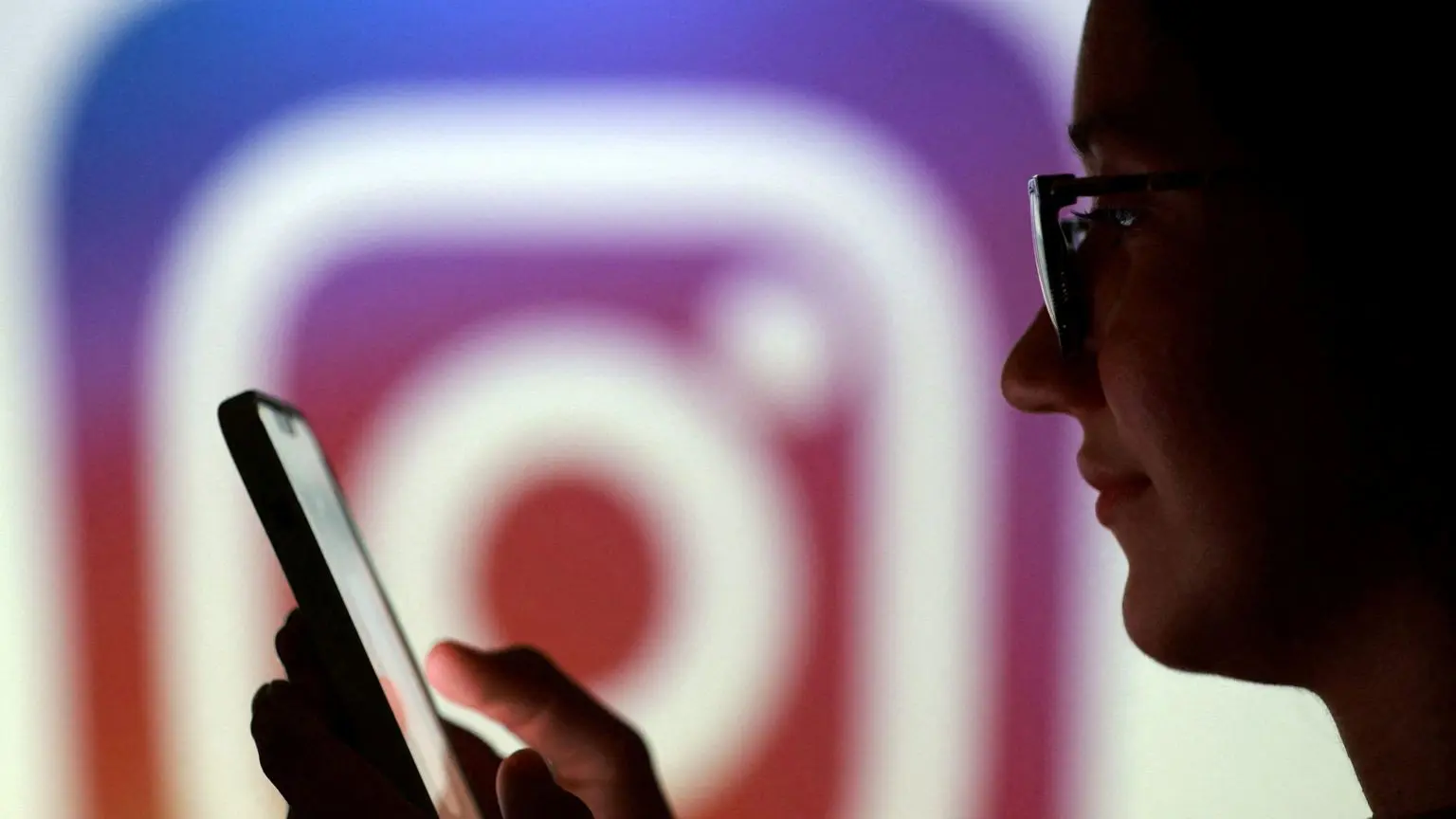 Владелец Instagram, компания Meta, планирует почти удвоить расходы на ИИ в этом году 1 Подросток позирует для фотографии, держа смартфон на фоне логотипа Instagram.