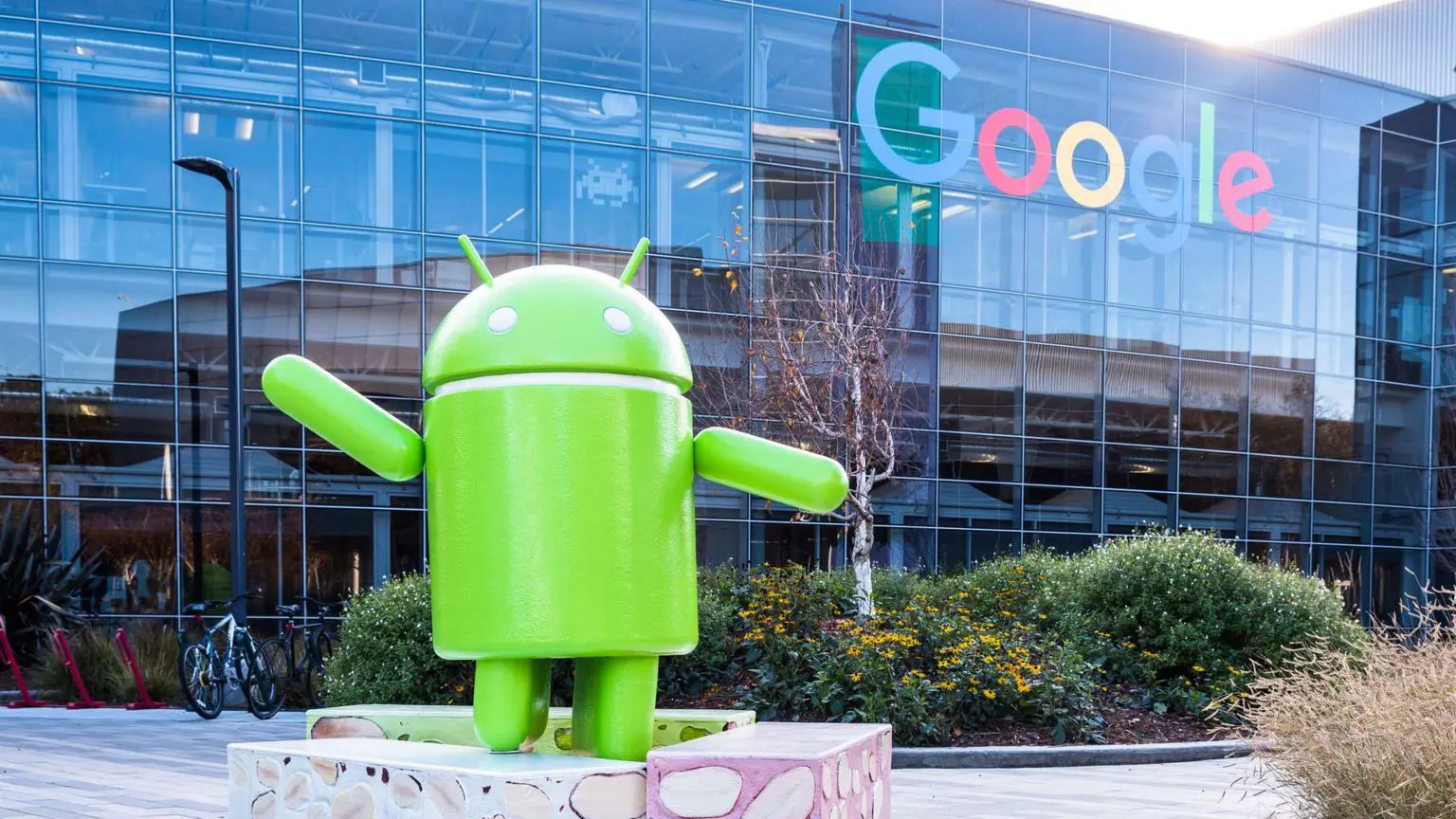 Google должен заплатить штраф в размере 4,1 млрд евро за использование Android для «блокировки» конкурентов. 1 Зеленый логотип Android в виде скульптуры, установленной снаружи стеклянного офисного здания Google, на котором также изображен логотип Google.